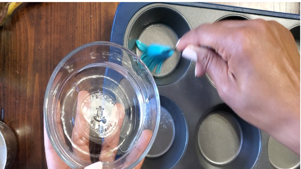 glass bowl of melted coconut oil being spread inside a muffin tin.