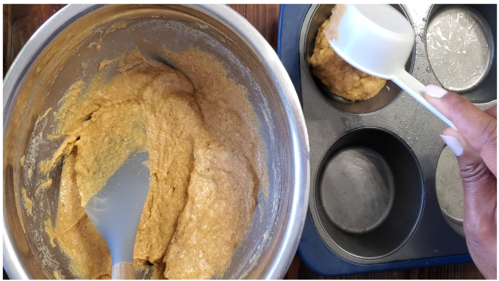 Measuring cup being used to put mixture into greased muffin pan