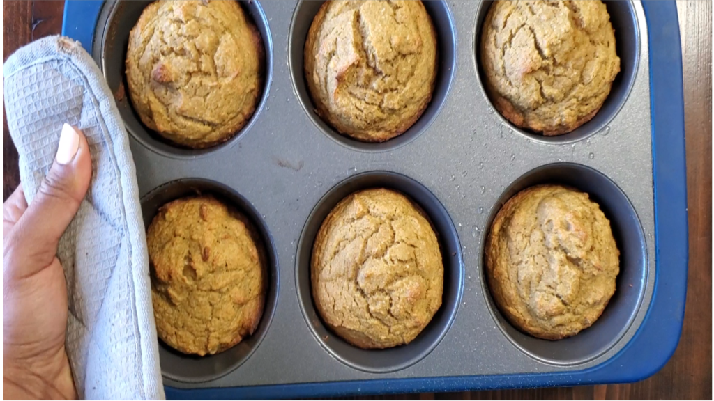 Hand holding golden muffins in a silver muffin pan.