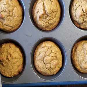 Hand holding golden muffins in a silver muffin pan.