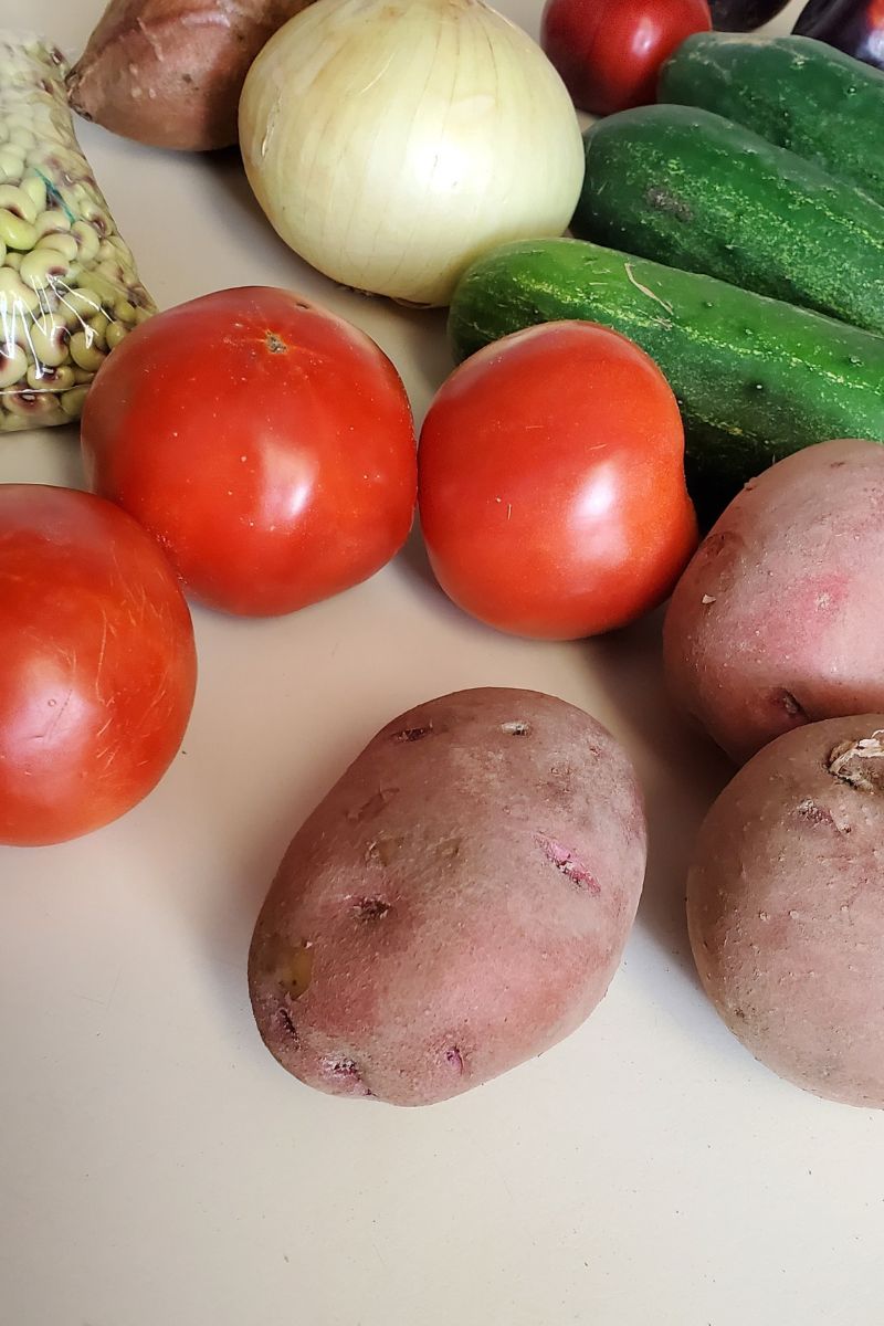 Picture of organic produce, tomatoes, red skinned potatoes, cucumbers, onion and beans. Style and Stewardship farmer's market produce haul.