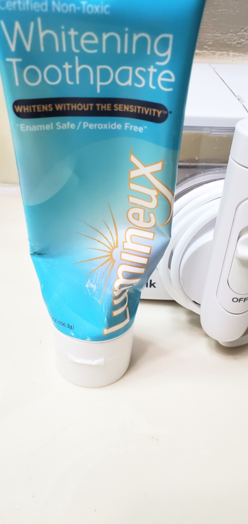 blue and white tube of Lumineux toothpaste sitting in front of a waterpik machine