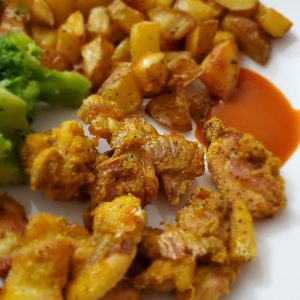 A plate with golden chicken nuggets, dipping sauce, golden potato cubes and broccoli style and stewardship