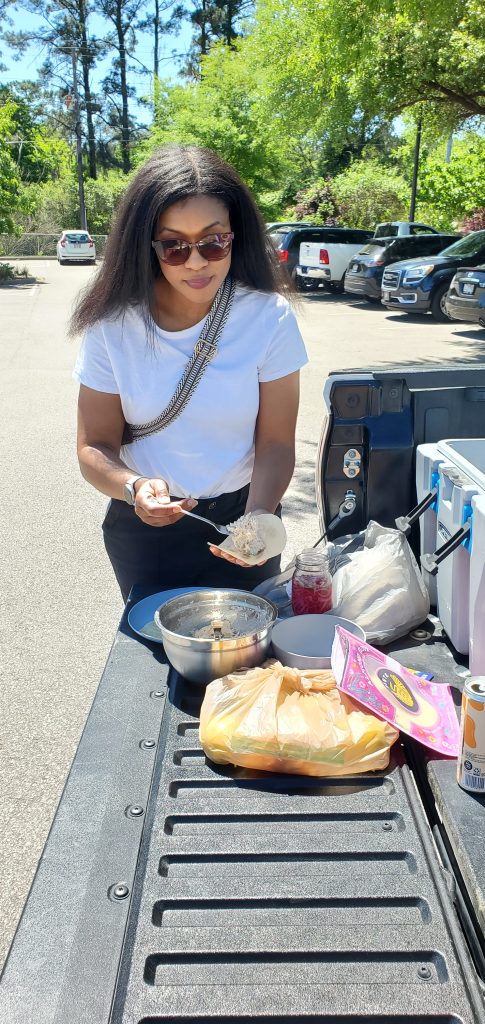 Woman wearing a white t shirt, sunglasses, with hair blowing in the wind while making a taco on the tailgate of a truck