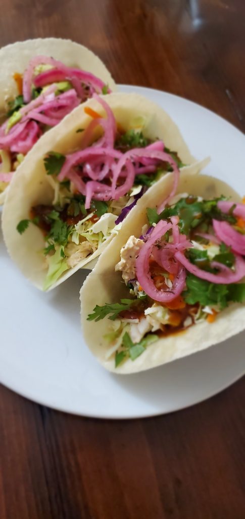 three tacos with shredded lettuce, cilantro, bbq sauce and pickled red onions