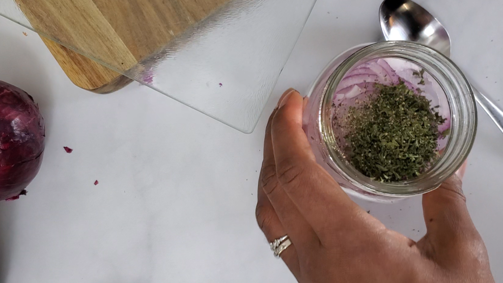 Small glass jar with red onions and topped with dried herbs