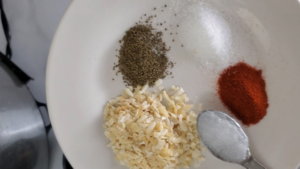 individual seasonings on a small white plate, smoked paprika, dried onion, salt, softened coconut oil, celery seed