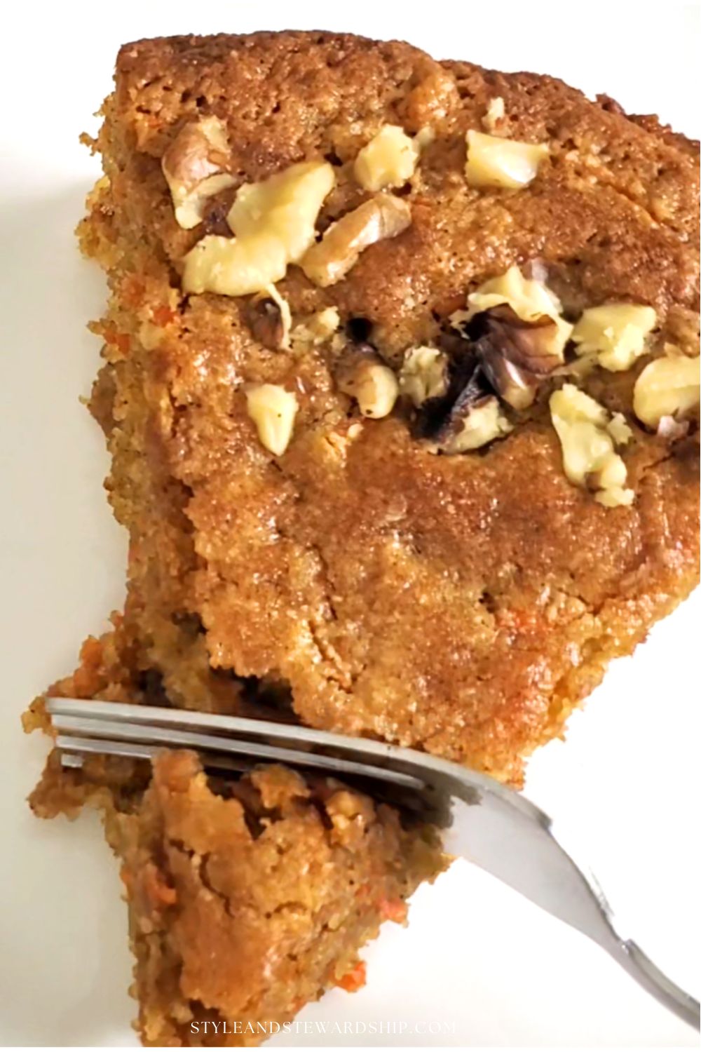 a slice of carrot cake with topped with walnuts on a small white plate. Cooling rack with carrot cake in the background style and stewardship dot com