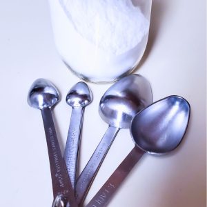glass jar with white baking powder and silver measuring spoons fanned out in front style and stewardship dot com
