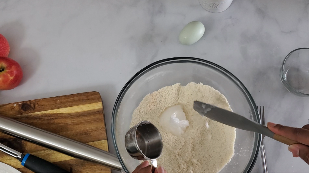 Adding softened coconut oil to a glass bowl that contains a grain free flour mixture