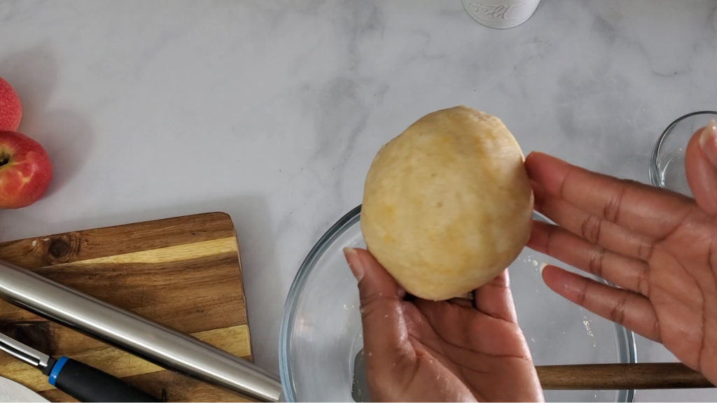 Hands holding a ball of pie dough over a glass bowl