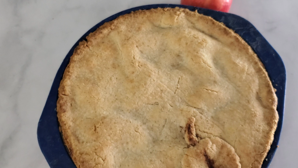 Apple pie in a blue rimmed pie pan with an apple on a counter