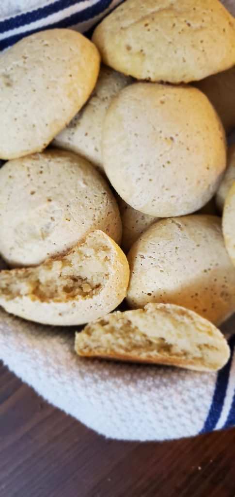 a stripped blue kitchen towel piled with gluten-free dinner rolls without rice a roll sliced open to reveal texture