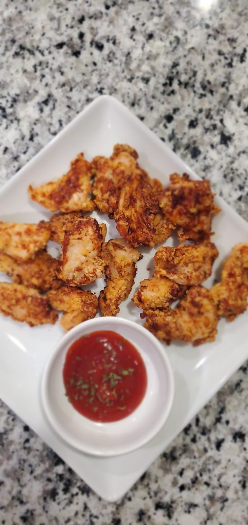 White square plate on top of a granite counter top with golden air-fried chicken nuggets, a small white condiment bowl with ketchup, and parsley on top. style and stewardship dot com