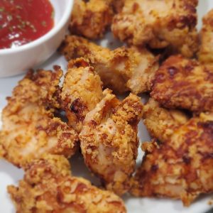 Golden air-fried chicken nuggets on a white plate with a white condiment bowl filled with ketchup and garnished with parsley. style and stewardship dot com