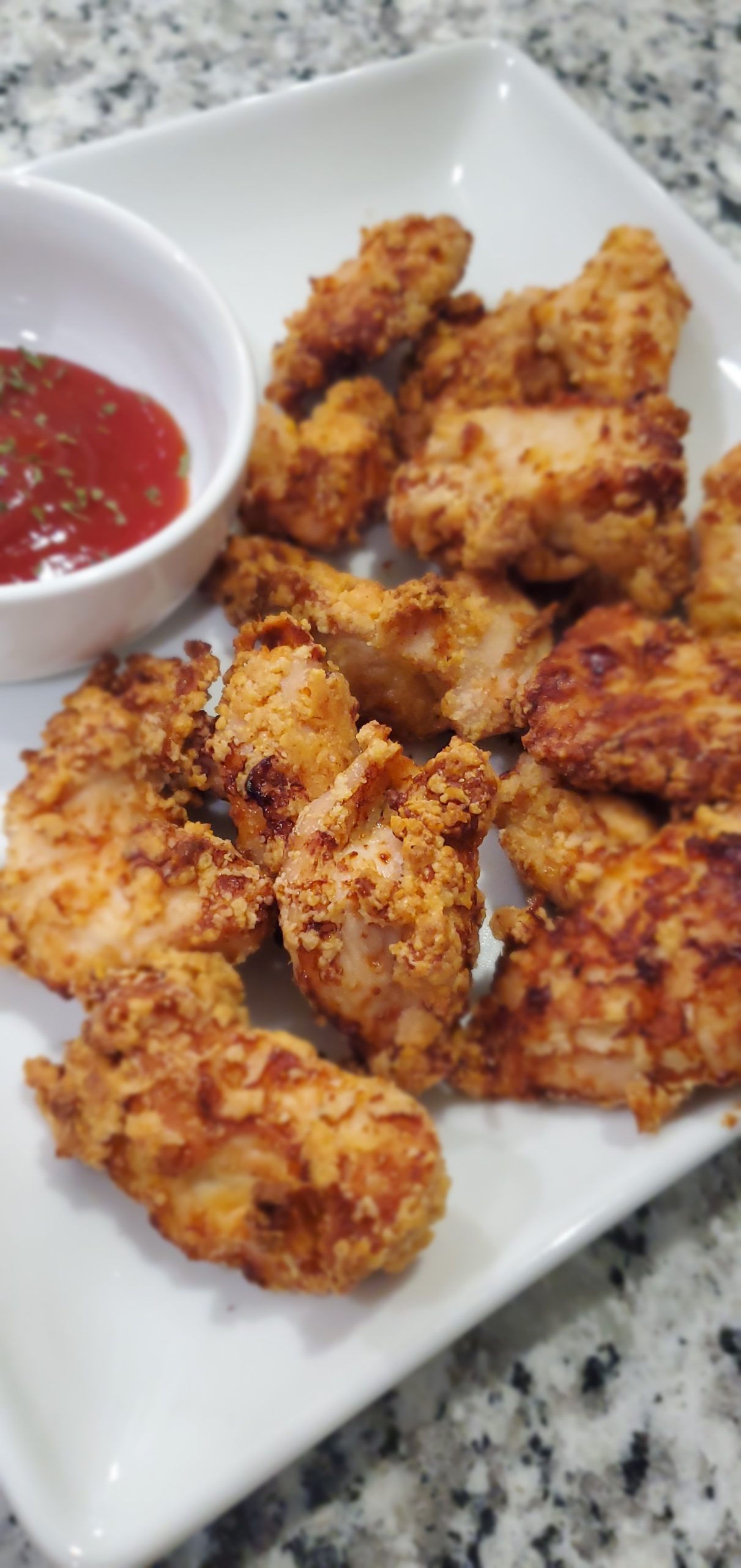 Golden air-fried chicken nuggets on a white plate with a white condiment bowl filled with ketchup and garnished with parsley. style and stewardship dot com