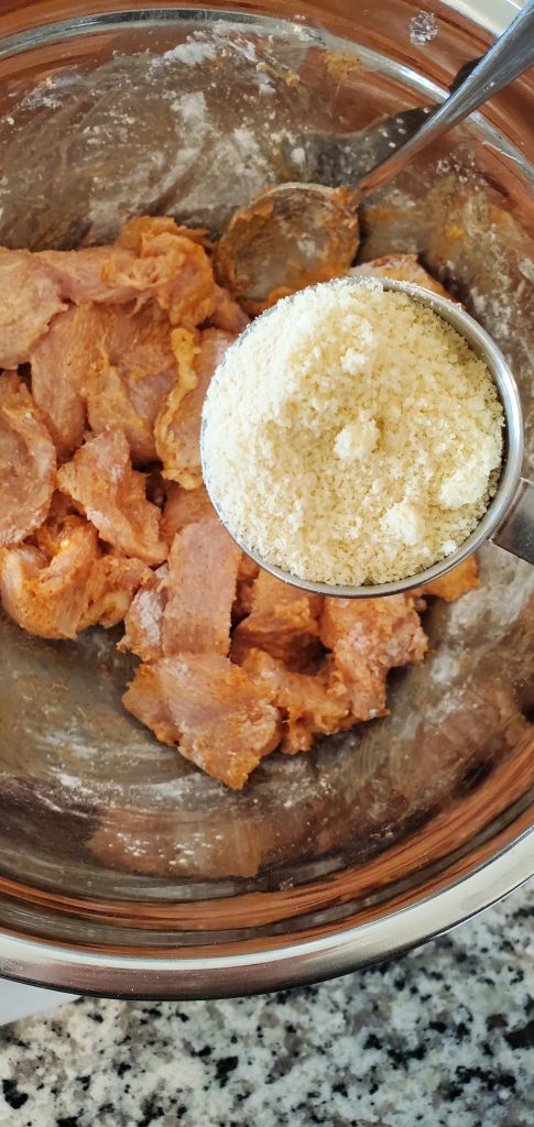 Stainless steel bowl with cut up chicken being topped with blanched almond flour. style and stewardship dot com