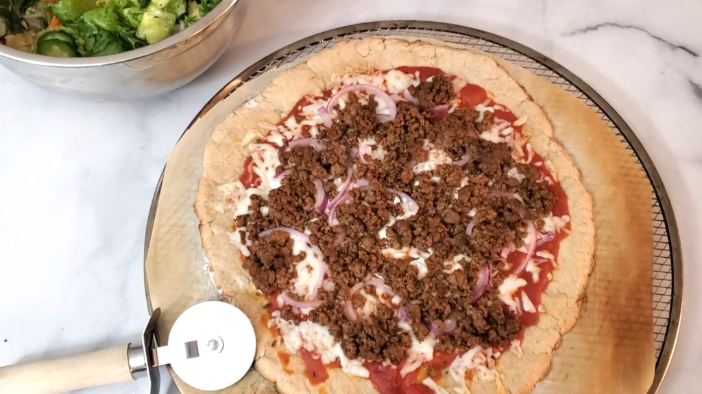 grain-free gluten-free pizza on top of dark parchment paper with a pizza cutter laying near by and a large bowl of salad 