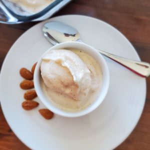 Almond milk ice cream in a small white bowl on top of a small white plate surrounded by whole almonds