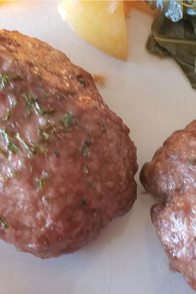 Two mini meatloaves on a white plate with potatoes and collards in the background. style and stewardship dot com