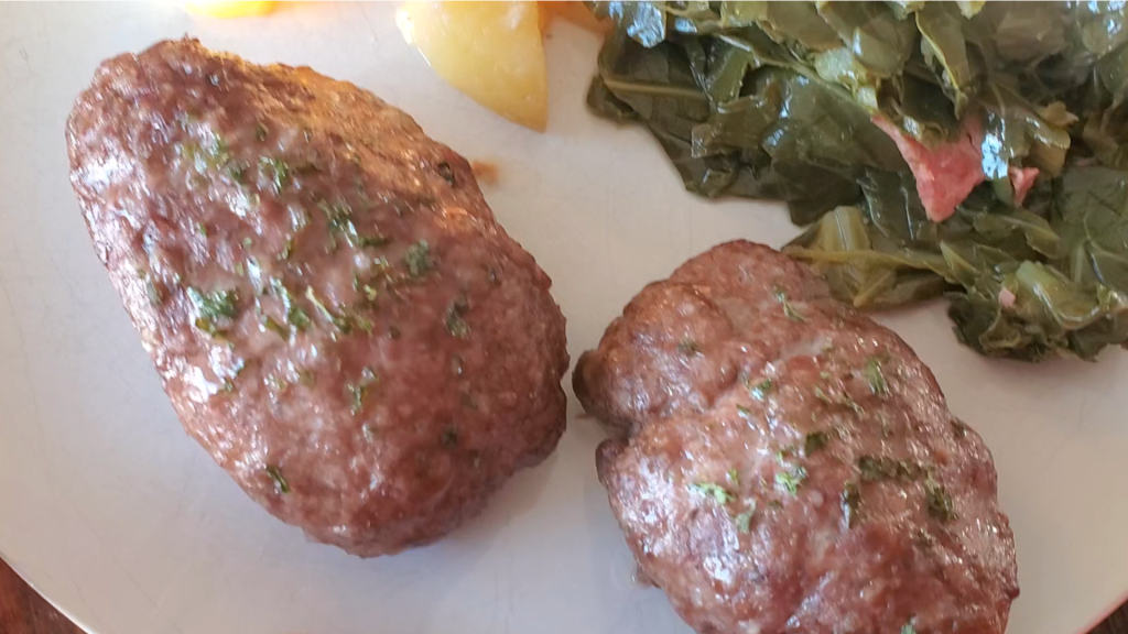 white plate with two small meatloaves next to greens and potatoes