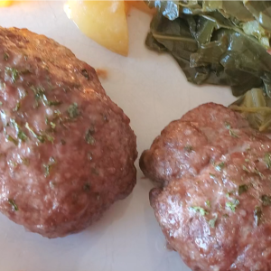 white plate with two small meatloaves next to greens and potatoes