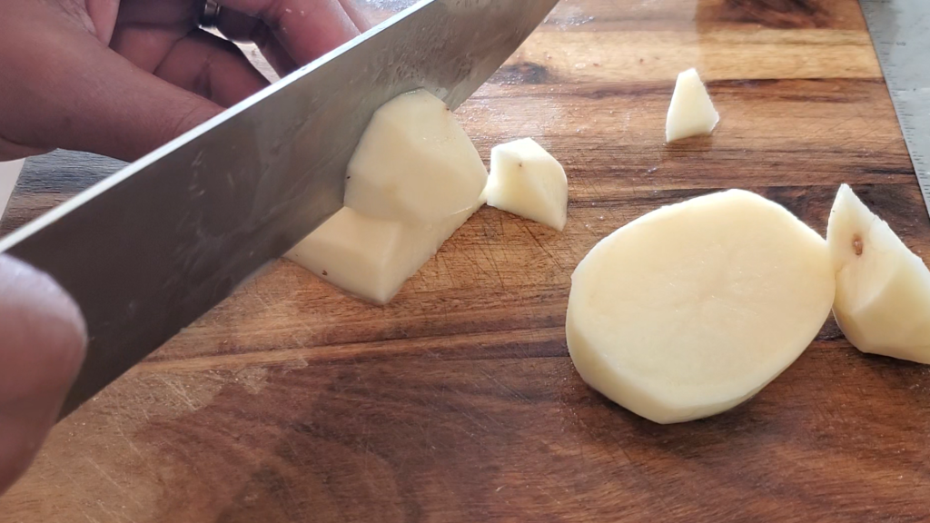 large knife cutting potatoes in cubes on a large dark wooden cutting board