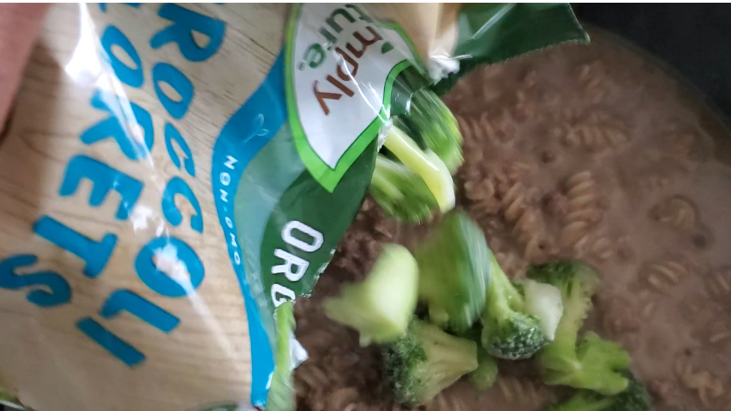 frozen broccoli being added to a pan with ground beef and gravy