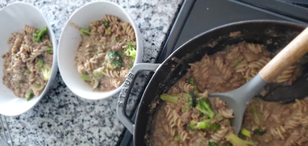large cast iron skillet with ground beef and broccoli next to two white bowls on a counter filled with the mixture