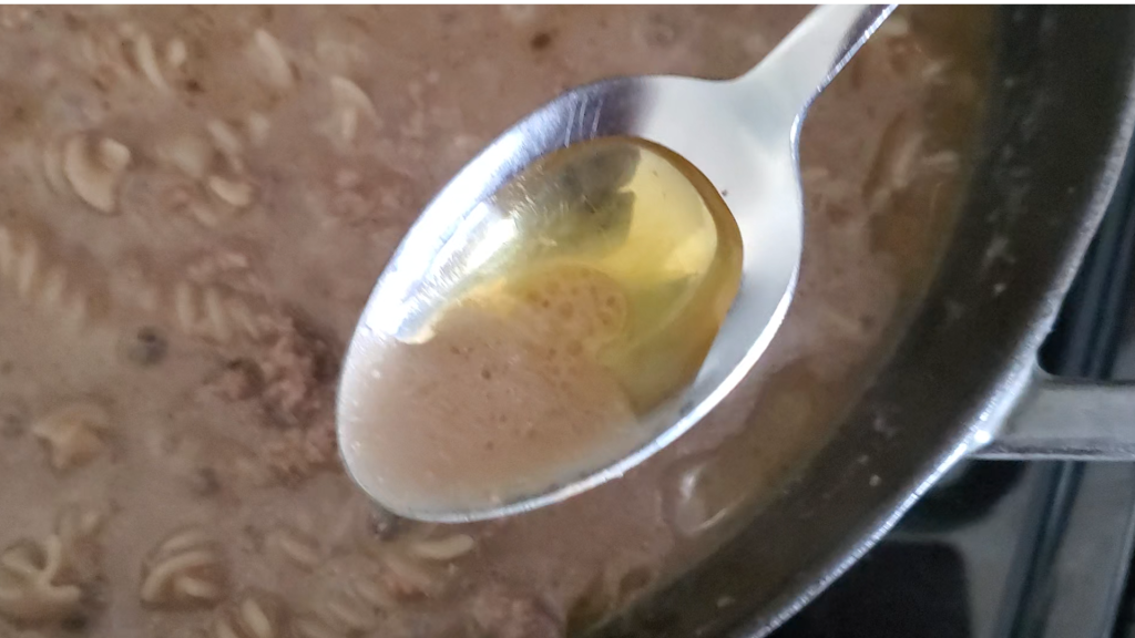 pan with ground beef and sauce and a spoon removing oil from the top