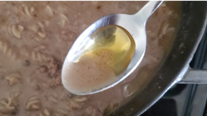 pan with ground beef and sauce and a spoon removing oil from the top