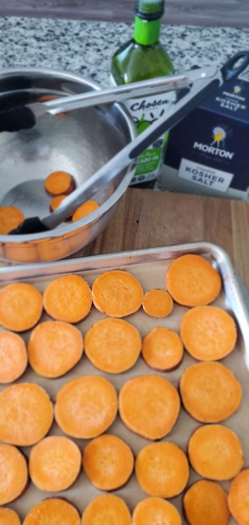 round sweet potato slices on a sheet pan lined with parchment and an avocado oil bottle is pictured with it