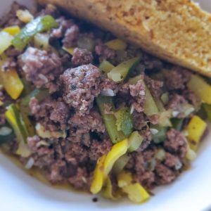 white bowl with yellow and green squash and ground beef and a side of cornbread
