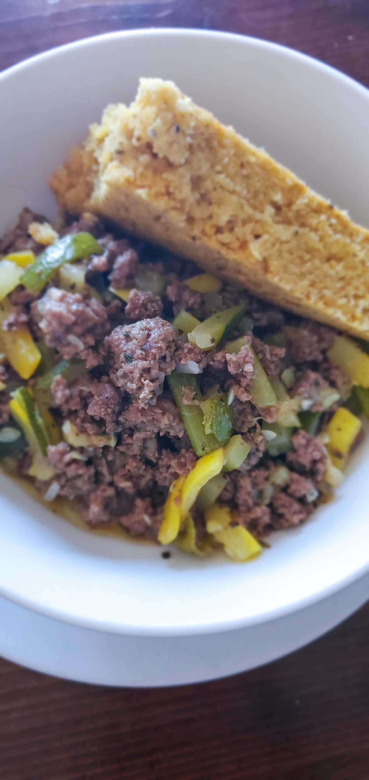 white bowl with yellow and green squash and ground beef and a side of cornbread