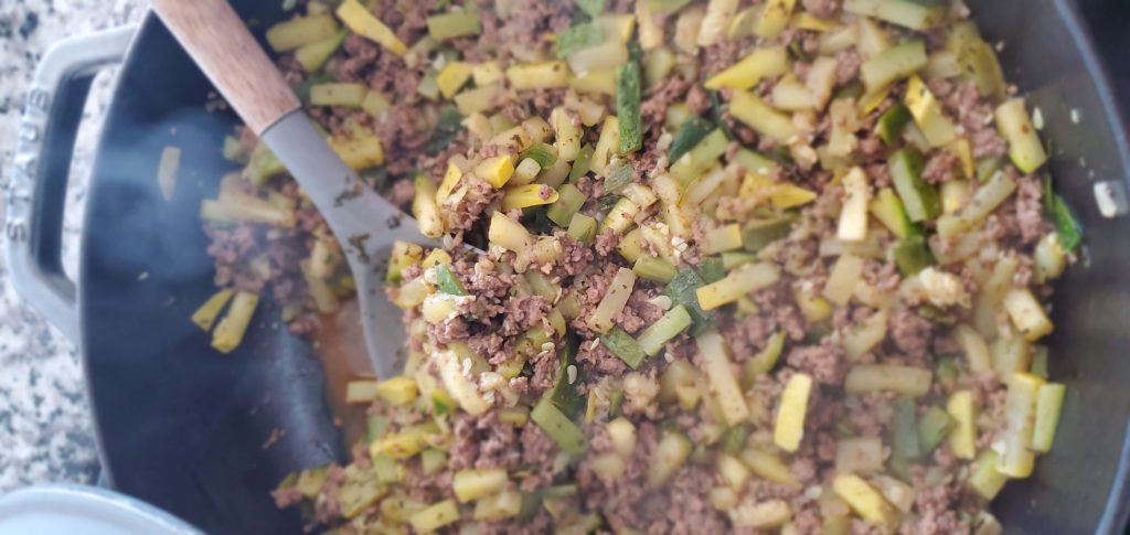 large skillet with wooden and silicone cooking utensil scooping yellow and green squash and ground beef