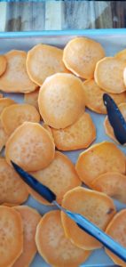 tongs and a pan laying out sliced and peeled sweet potatoes