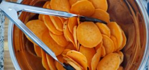 a large set of tongs and stainless steel bowl with sliced sweet potatoes