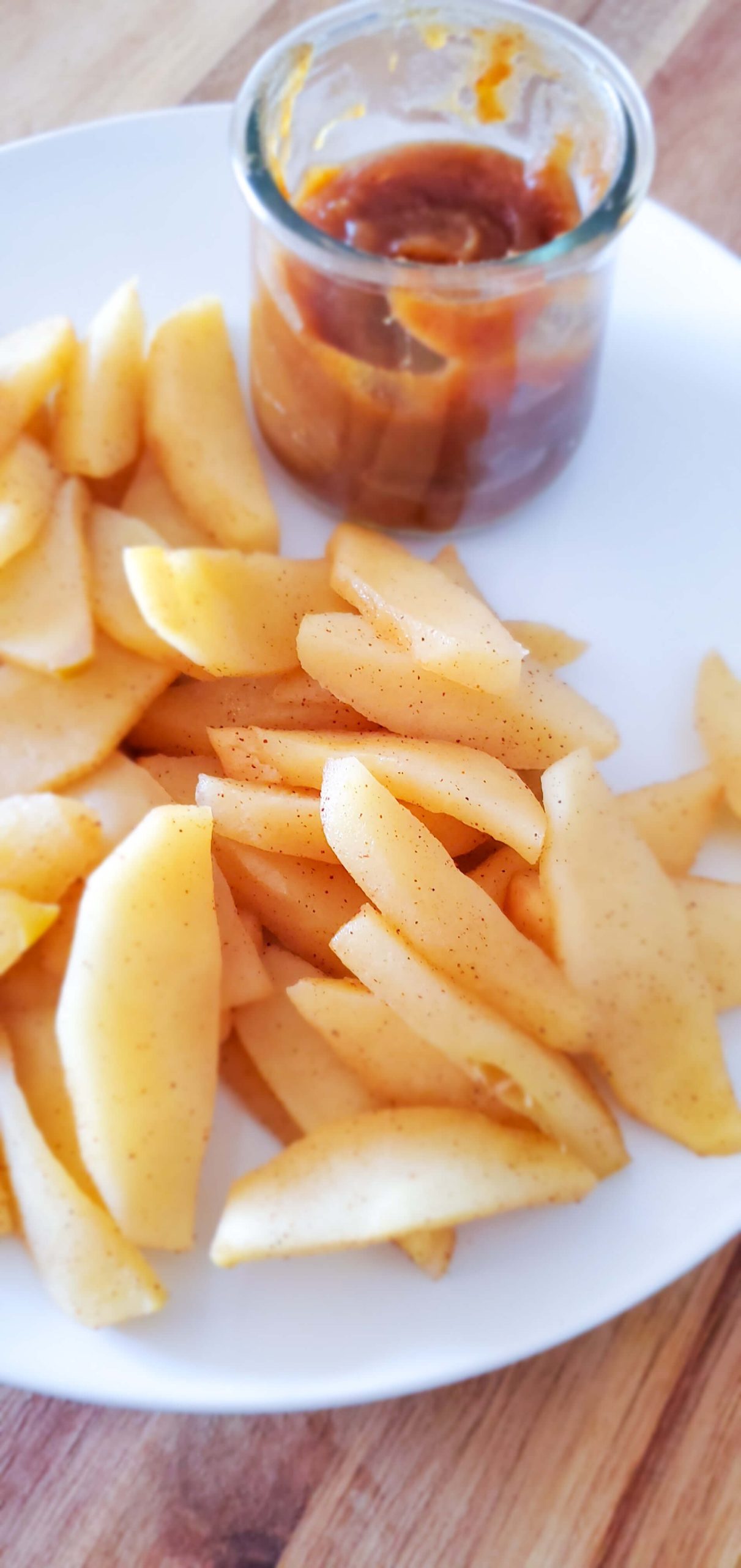 Sliced apples on a white plate and small glass bowl with date caramel dip