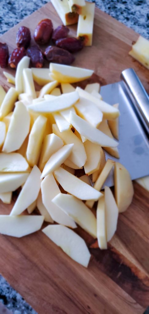Slices of apples on a large wooden cutting board and dates on the side