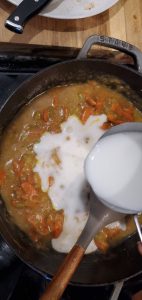 a measuring cup of milk being poured into a skillet with carrots and celery