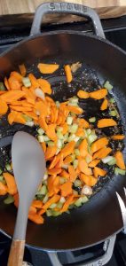 carrots and celery in a large skillet pictured with a wooden spoon stirring the mixture
