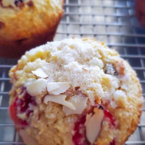 Cranberry orange muffin with sliced almonds and sugar crystals on top cooling on a metal rack style and stewardship dot com