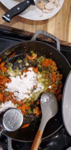 flour being added to a carrot and celery mixture