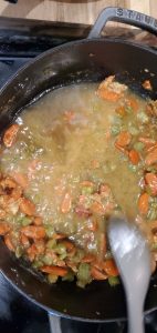 stock being added to a skillet with carrots and celery