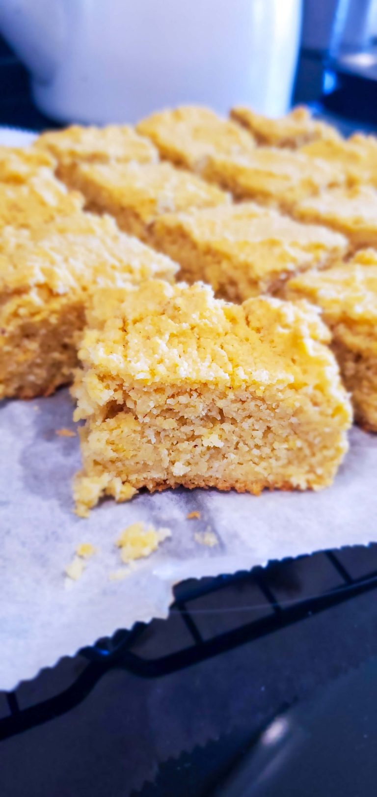 Golden squares of baked cornbread sitting on top of parchment paper with small bits of crumb around.