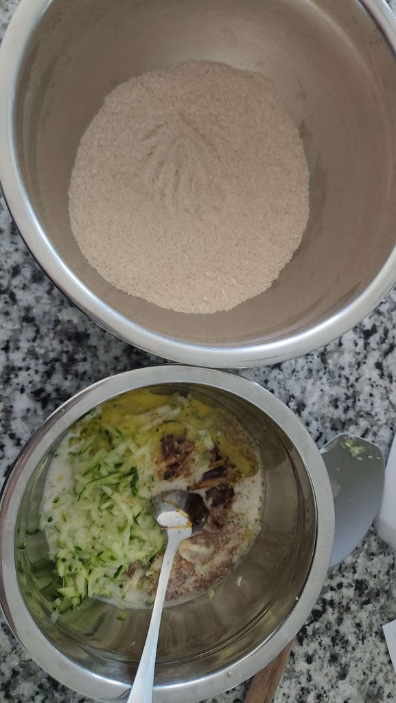 two stainless steel bowls with dry mixture in one and wet mixture and grated zucchini in the other