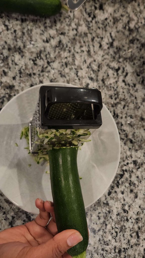 a white bowl beneath a zucchini that is being grated 