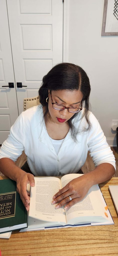 Cher of Style and Stewardship wearing a white top and looking down at an open book on a desk