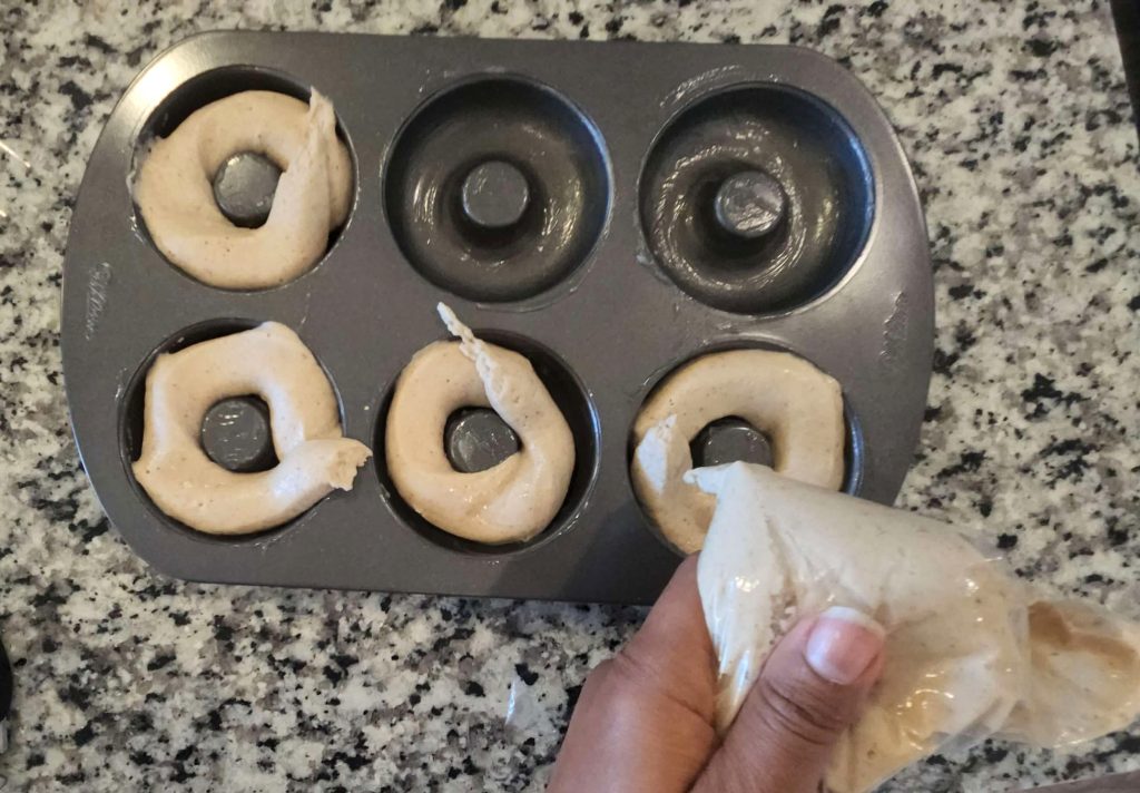 Batter being piped into a doughnut pan.