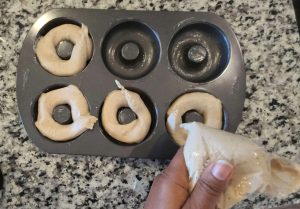Batter being piped into a doughnut pan.